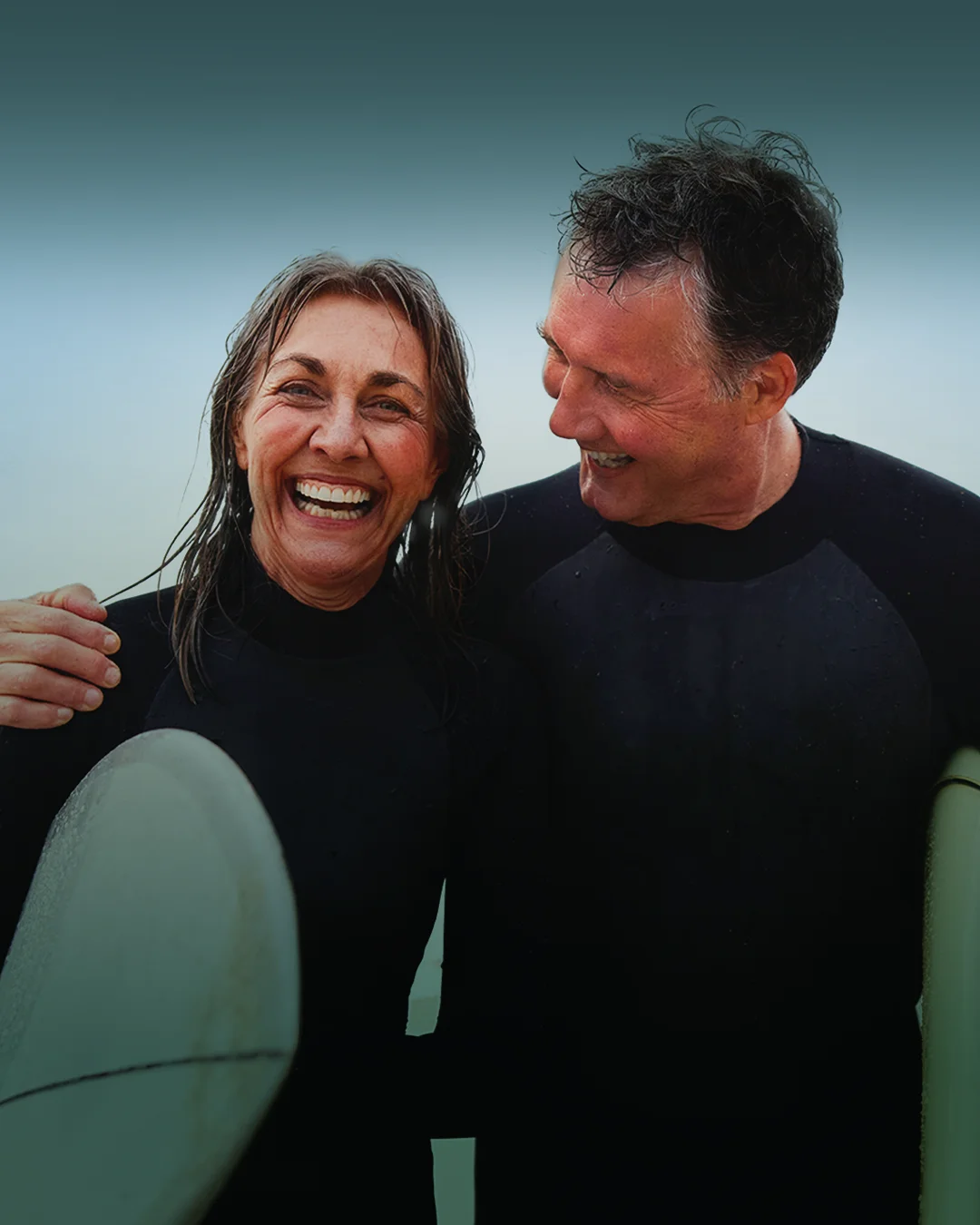Porträt eines fröhlichen älteren Surferpaares mit Surfbrettern, Mann mit Arm um Frau - Stock-Fotografie