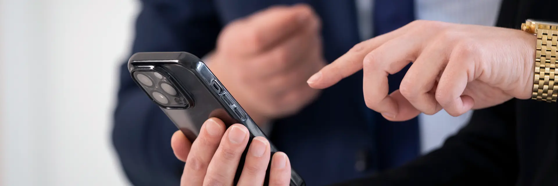 Person bedient ein Smartphone mit dem Finger und zeigt einer anderen Person etwas darauf