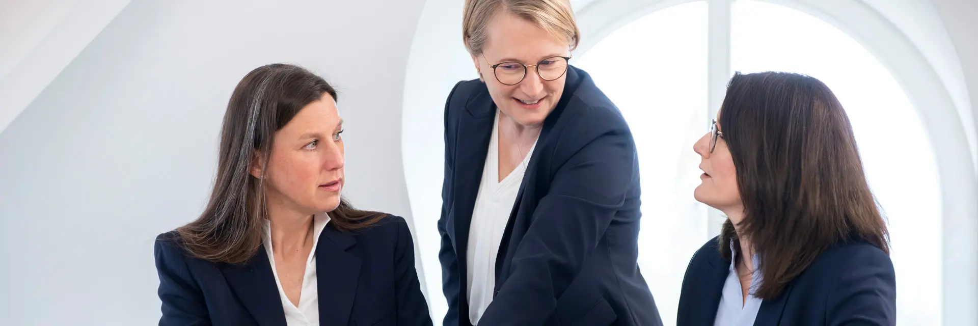 Eine Frau erklärt ihren Kolleginnen etwas, während diese am Tisch sitzen