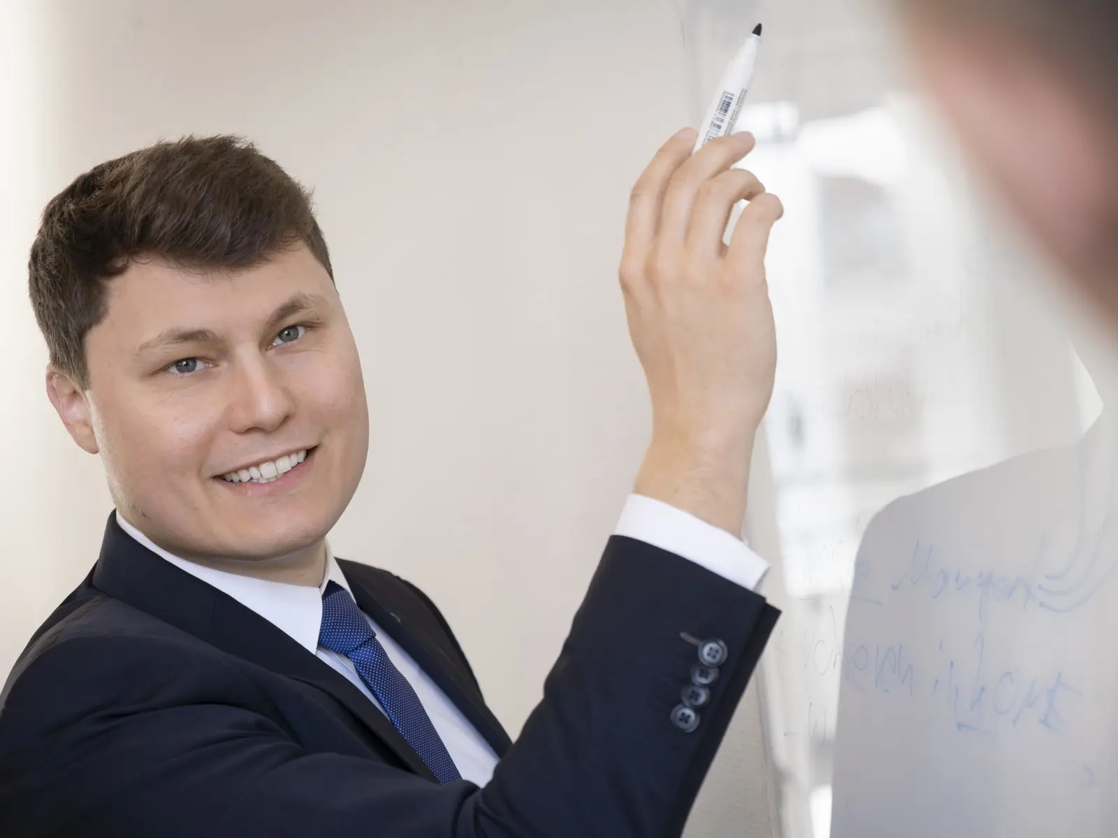 Ein Mann im Anzug schreibt lächelnd auf ein Whiteboard.