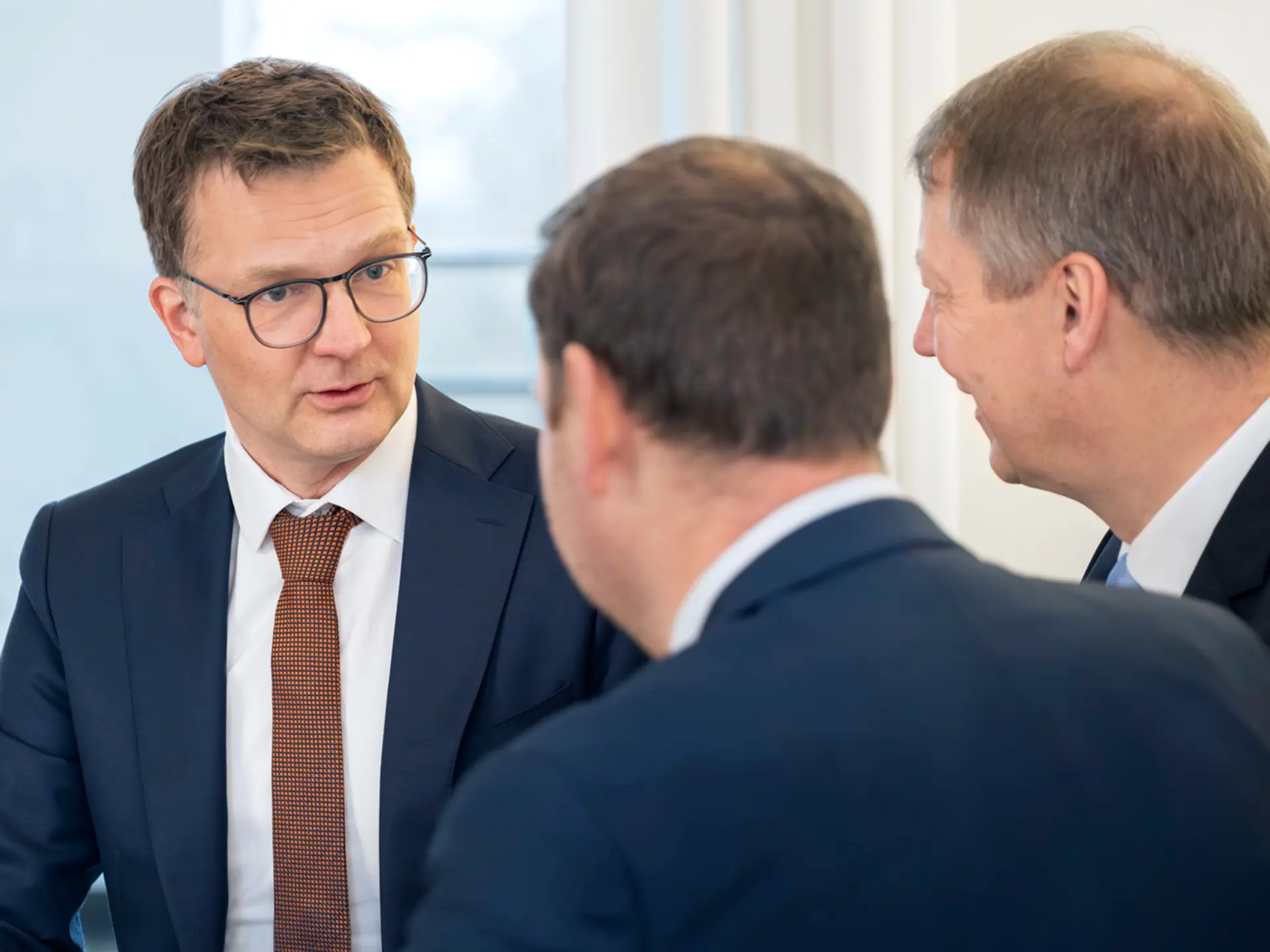 Drei Personen in Anzügen unterhalten sich ernst