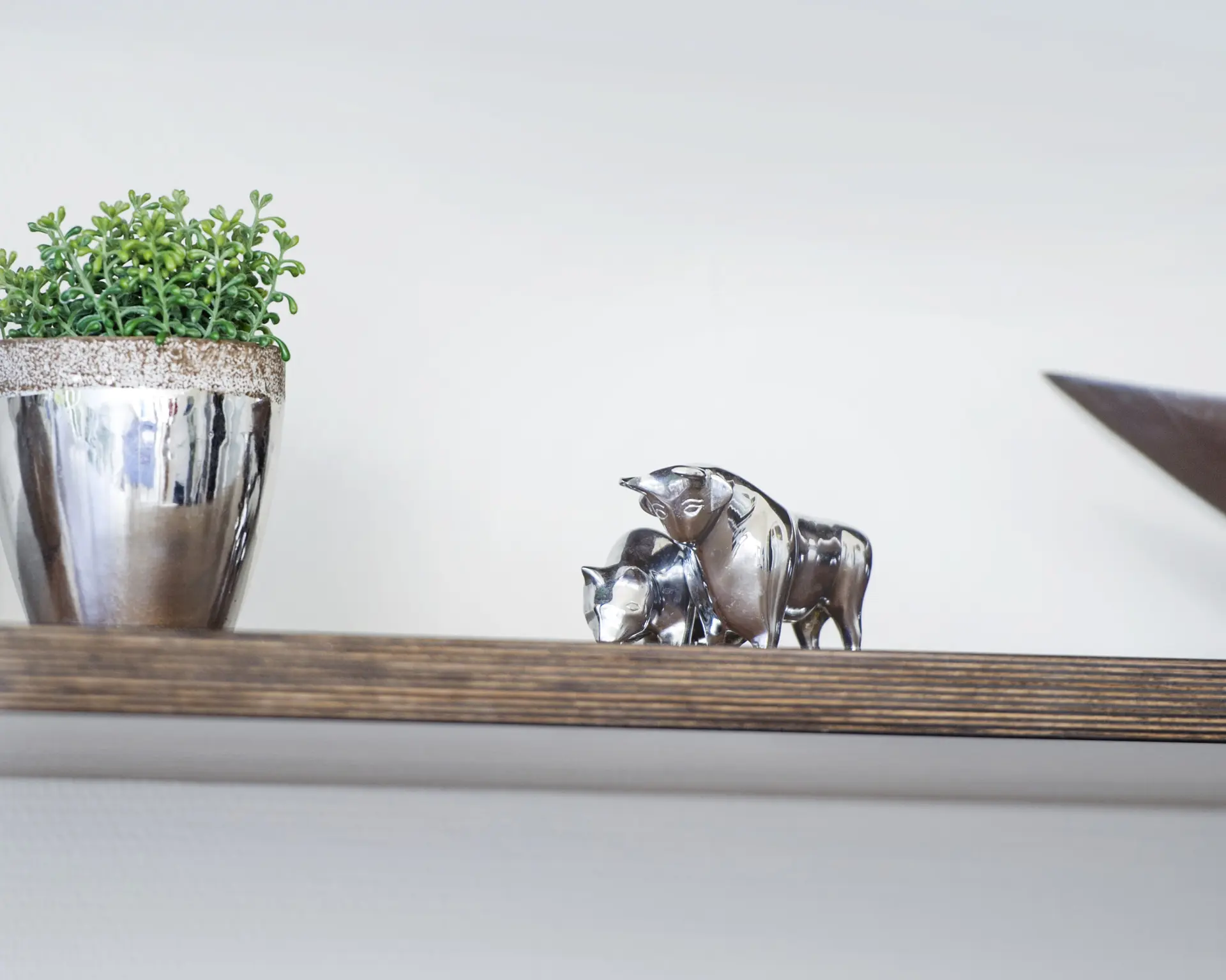 Silberne Stier- und Bärenfiguren auf einem Holzregal neben einem Pflanzentopf