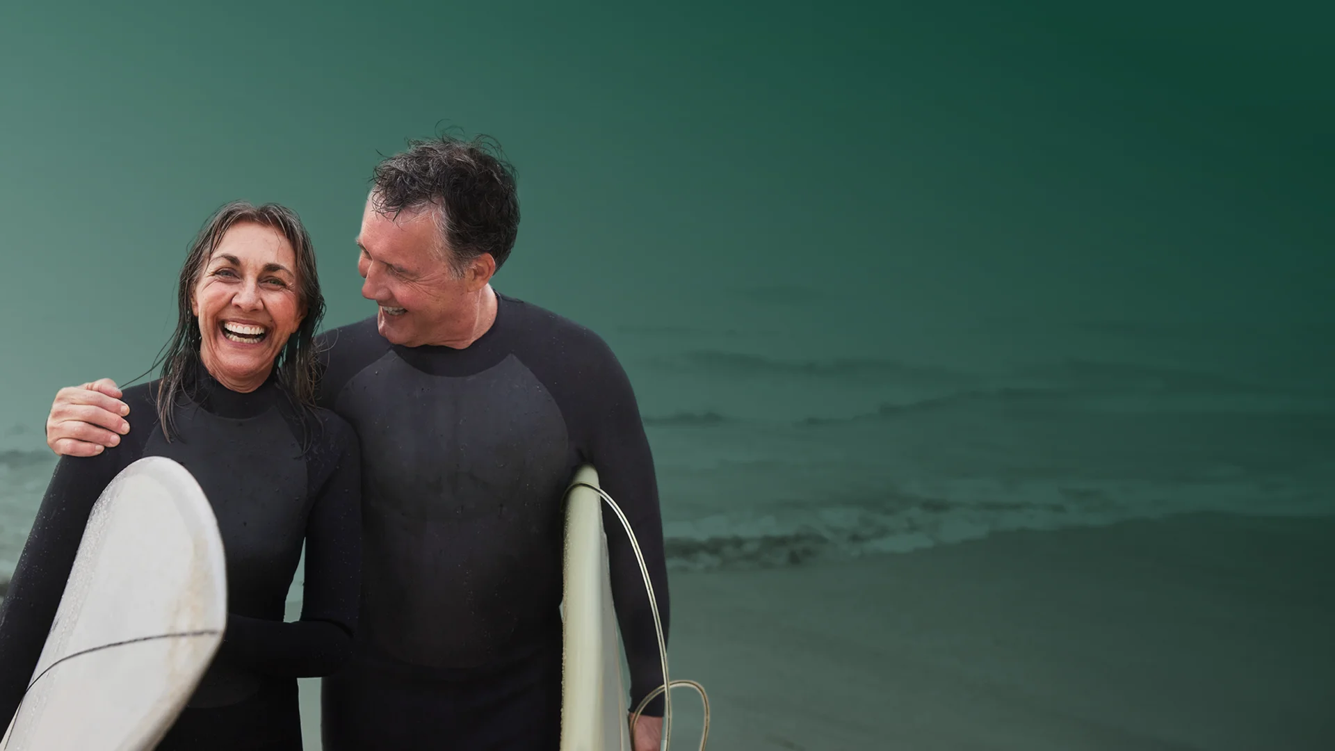 Porträt eines fröhlichen älteren Surferpaares mit Surfbrettern, Mann mit Arm um Frau - Stock-Fotografie