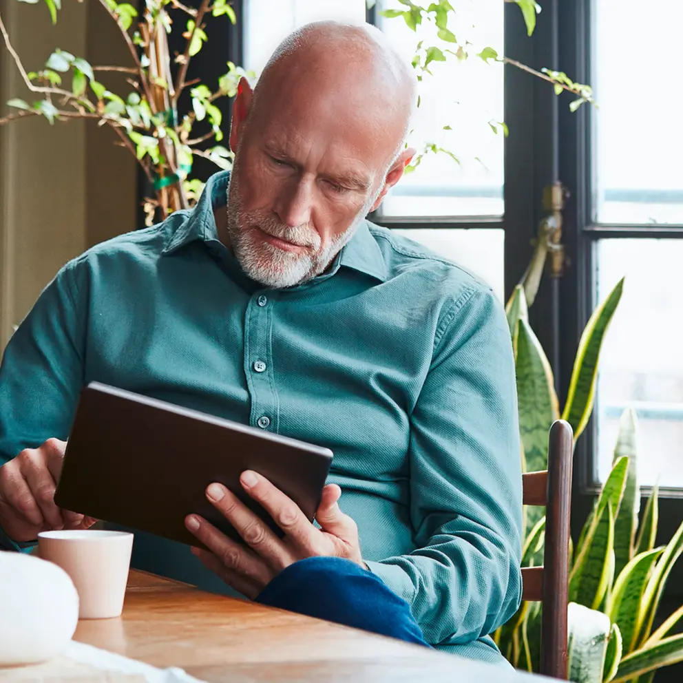Älterer Mann nutzt ein digitales Tablet am Tisch