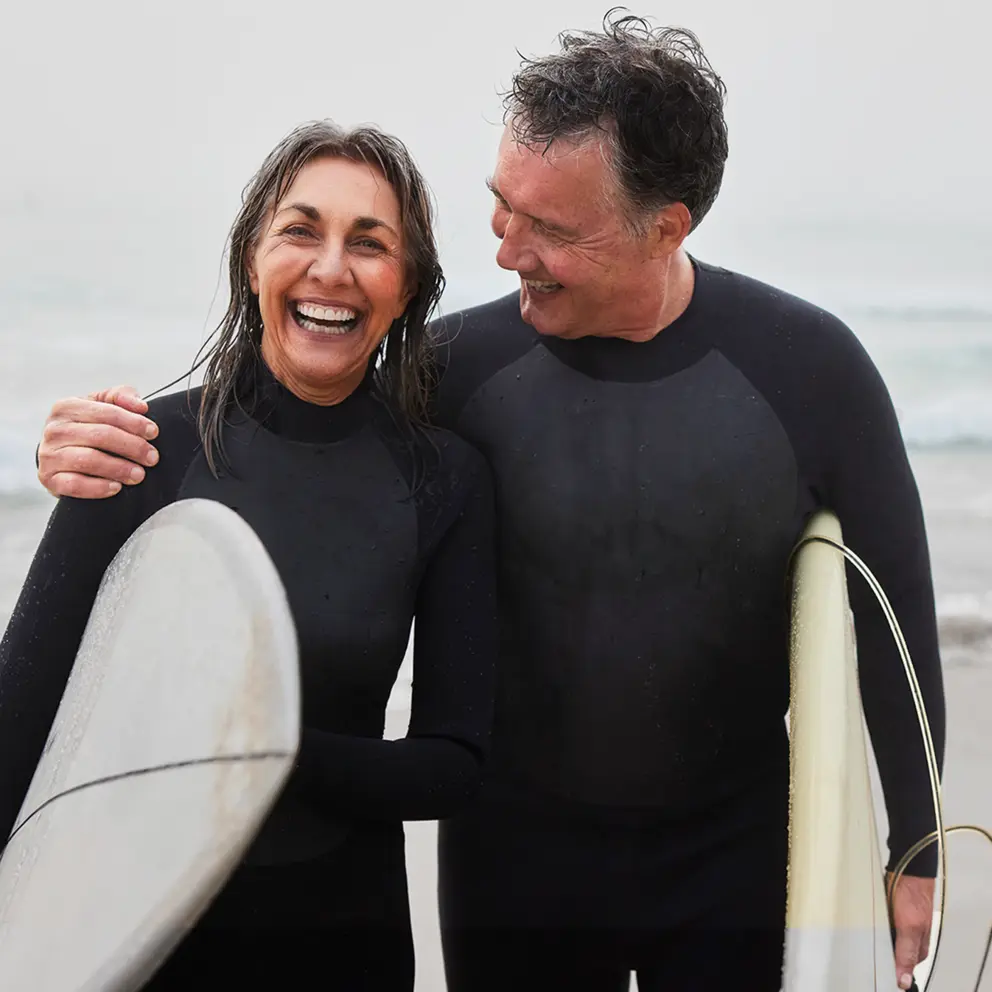 Porträt eines fröhlichen älteren Surferpaares mit Surfbrettern, Mann mit Arm um Frau - Stock-Fotografie