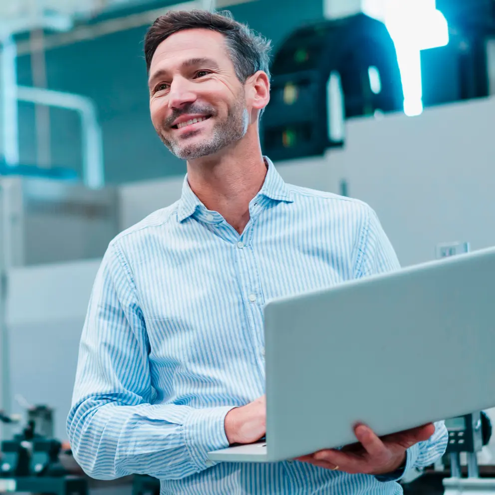 Ein lächelnder Mann steht in einer modernen Arbeitsumgebung und hält einen Laptop in der Hand