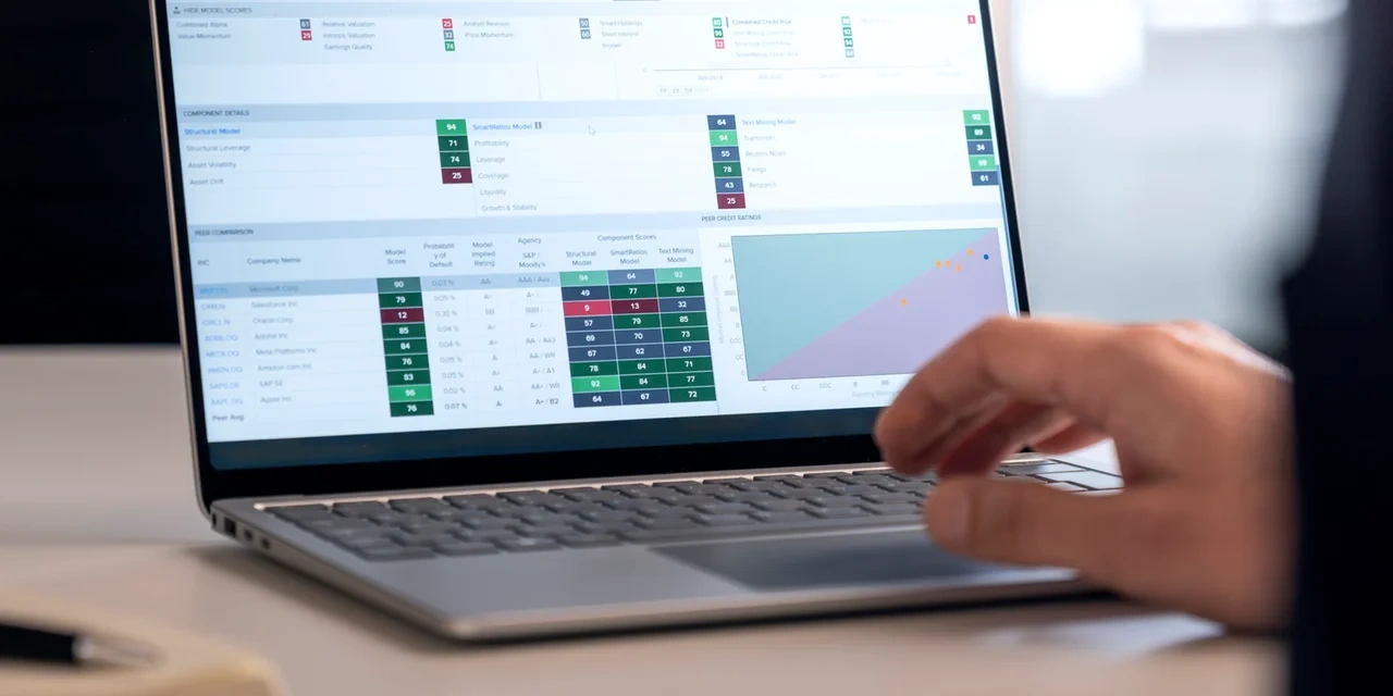 Eine Hand bedient ein Laptop mit einer Finanzanalyse-Oberfläche, die Tabellen, Bewertungen und Diagramme zeigt.