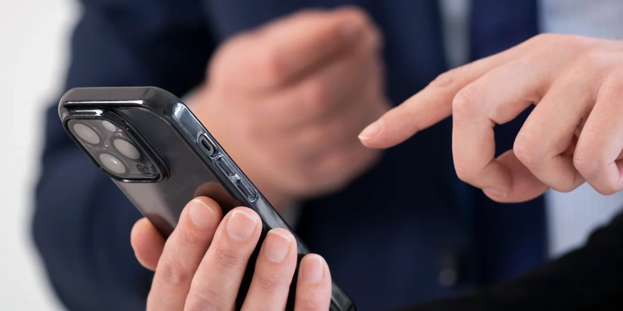 Person bedient ein Smartphone mit dem Finger und zeigt einer anderen Person etwas darauf