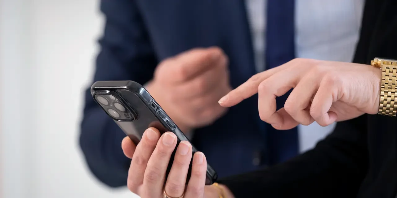 Person bedient ein Smartphone mit dem Finger und zeigt einer anderen Person etwas darauf