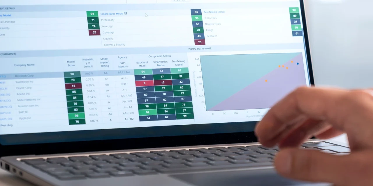 Eine Hand bedient ein Laptop mit einer Finanzanalyse-Oberfläche, die Tabellen, Bewertungen und Diagramme zeigt.