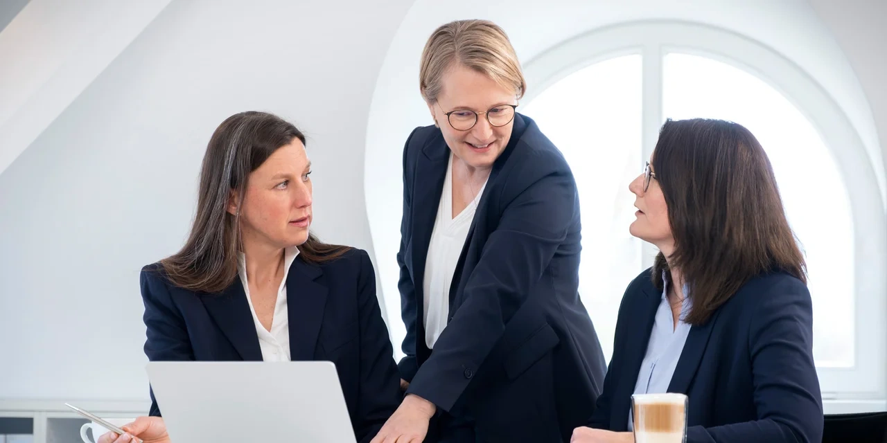 Eine Frau erklärt ihren Kolleginnen etwas, während diese am Tisch sitzen