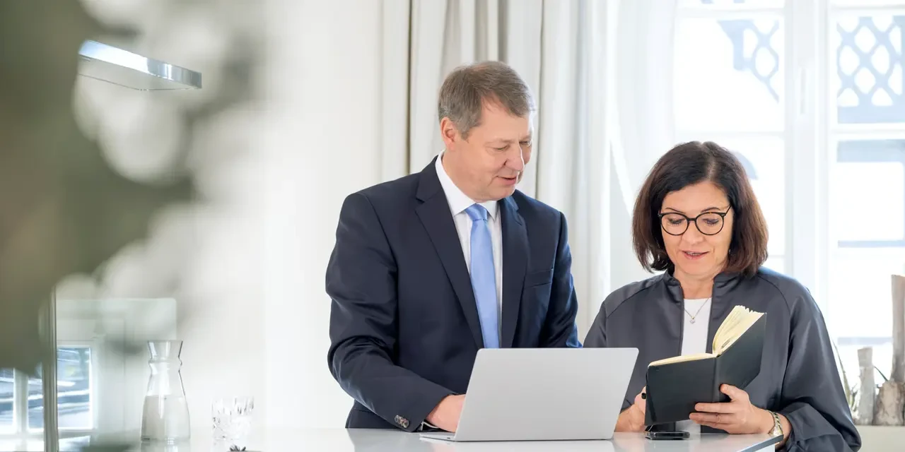 Mann und Frau stehen gemeinsam an einem Stehtisch und schauen auf Laptop und Notizbuch 